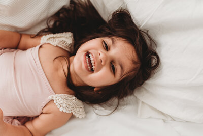 Brown haired three year old laying on the bed and laughing