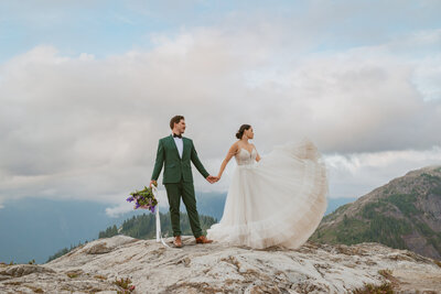 Groom and bride stand top of Mount Baker and play with her dress