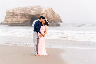 Man and pregnant wife embracing on a  Santa Cruz Beach