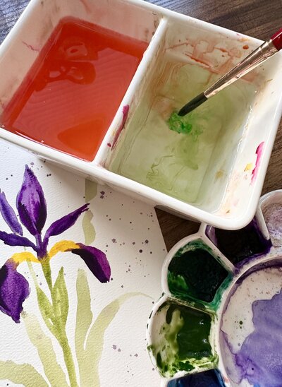 Colorful iris watercolor painting and water cups and paint brush on a table