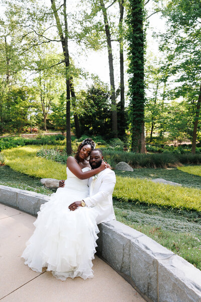 black couple sitting in a botanical garden holding each other with their eyes closed.