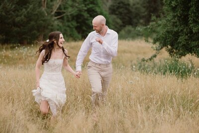 Couple running through grassy smiling at each other at their wedding.
