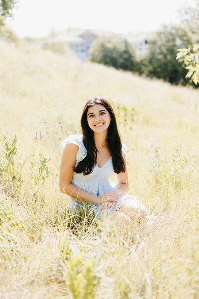 Senior girl in a blue dress sitting in a bright grassy field