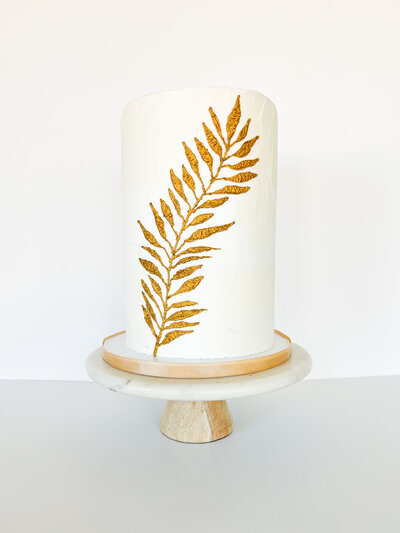 White wedding cake with gold leaf sitting on a marble cake stand.
