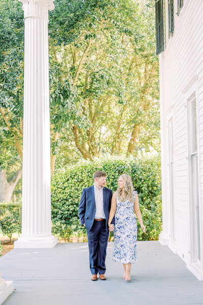 Engaged couple holding hands standing on porch with large white columns