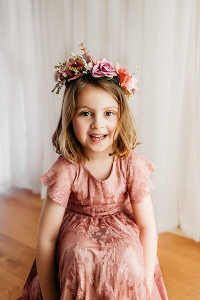 toddler smiling at camera in rose colored dress with flower crown