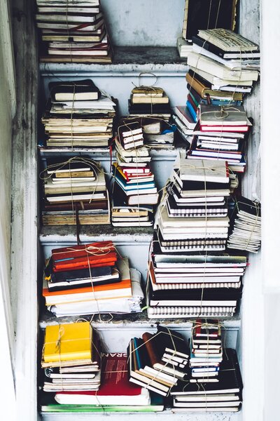 Stacks of notebooks bound by twine, piled on white stairs. Photo by Julia Joppien via Unsplash.