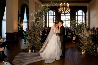 Bride and groom kiss inside the Ebell of Los Angeles at their whimsical ceremony in the round.