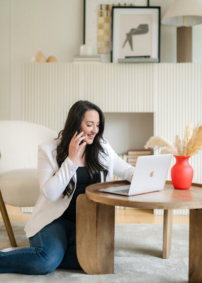 woman sitting in a white blazer speaking on her phone