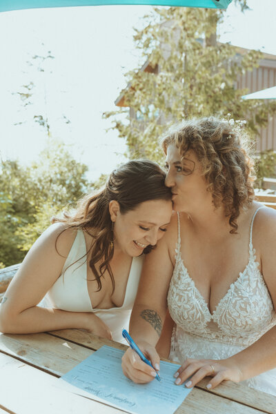 Two brides signing their wedding certificate during a PNW wedding, captured by Bare Bones Photo