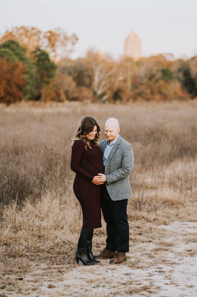 Couple hold pregnant woman's baby bump in a Raleigh NC field during maternity session by Worth Capturing photography