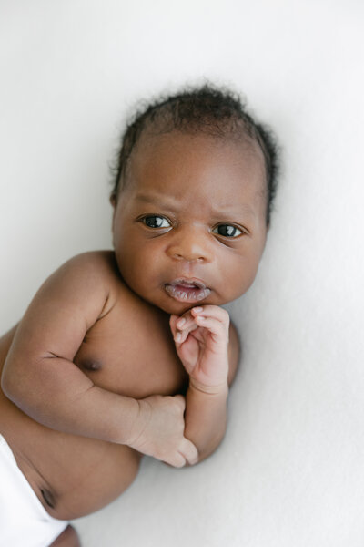 Newborn baby boy lies with his hand under his chin during newborn photography session