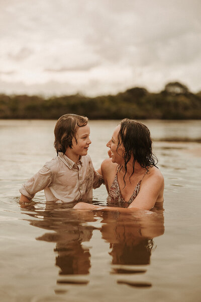 Candid family photo of a mother and son laughing together in the water, captured by Sunshine Coast photographer.