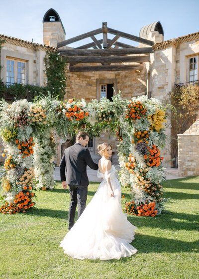 A newlywed couple in front of a stunning floral arch at Sunstone Winery in Santa Ynez California