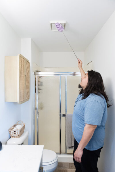 Professional cleaner dusting vent in bathroom