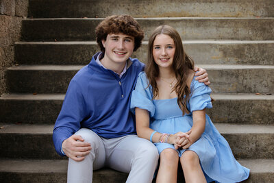 Charlotte photographer captured photo of siblings on concrete steps smiling at the camera wearing hues of blue for their family portrait session.