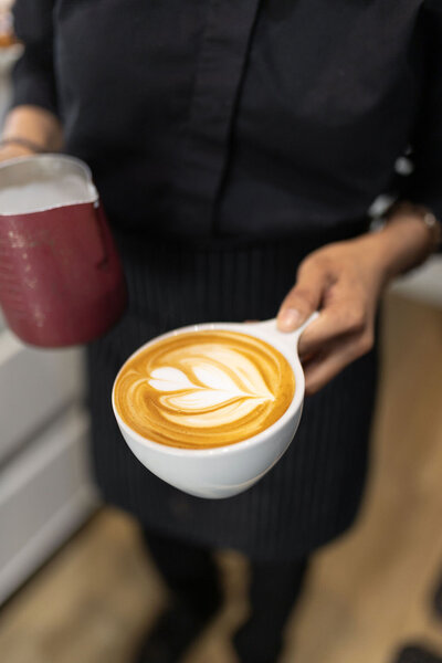 Close-up of a barista holding a latte with heart-shaped foam art at Gold Leaf Pastries in Kamloops BC.