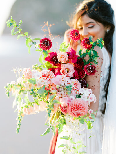 Bride holds big bridal bouquet with magenta and pink florals at Cannon Beach haystack Rock in Oregon