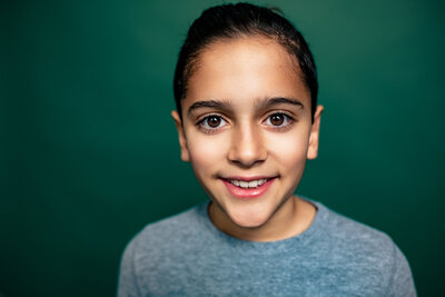 A preteen boy poses at the senior photos pittsburgh studio in a compelling portrait where his large Brown eyes stand out against a dark green background.