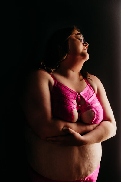 stunning image of a woman in a bright pink bra hugging herself and taking a deep breath in a Oshkosh boudoir studio