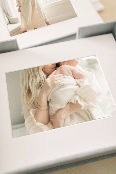 Close-up of a professionally printed and matted photograph showing a Kansas City mother snuggling her newborn, part of a custom album by Meredith Maag Photography.
