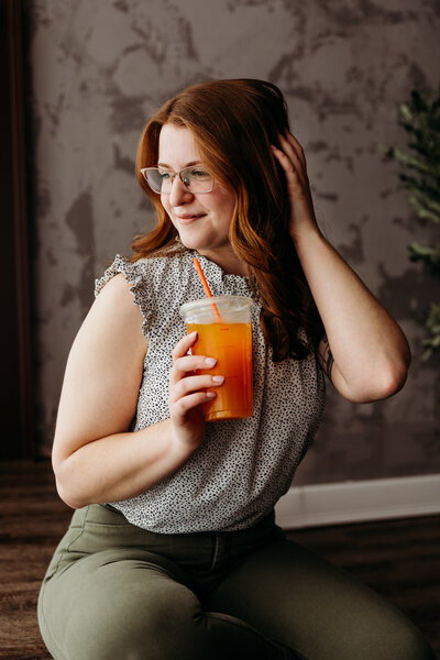 Photo of a woman sitting down, holding an iced drink with a straw.