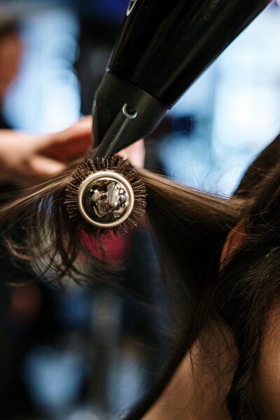 Closeup of a round brush and hair dryer being used on long hair.