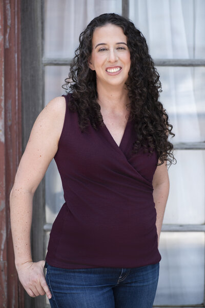 A person smiling with their hands hooked in their back pockets 