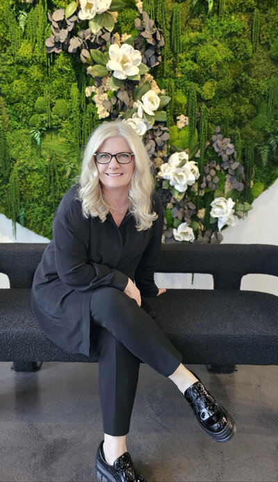 Teriva seated on couch smiling in front of floral wall.