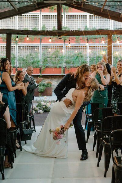 Groom dips bride in the aisle after saying "I do" while crowd cheers them on.