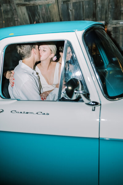 Flash photo of bride and groom kissing in a vintage blue and white truck