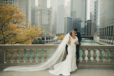 bride and groom standing on bridge in chicago with bride wearing cathedral veil