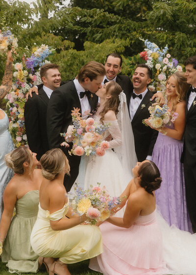 Bride and groom kiss surrounded by their colorful wedding party