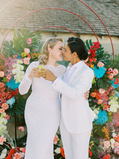 LGBTQ brides kissing and cheers with cocktails