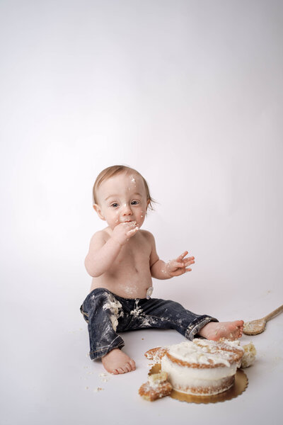 little girl sitting a blue star romper while eating cake for her one year cake smash