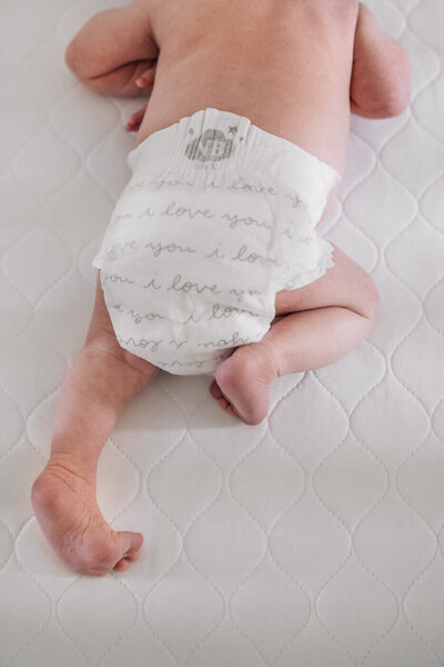 A tiny baby lies in his crib on his tummy wearing his newborn size diaper.