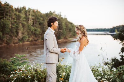 Bride and groom holding hands during their Portland Maine wedding ceremony overlooking the river and forest.