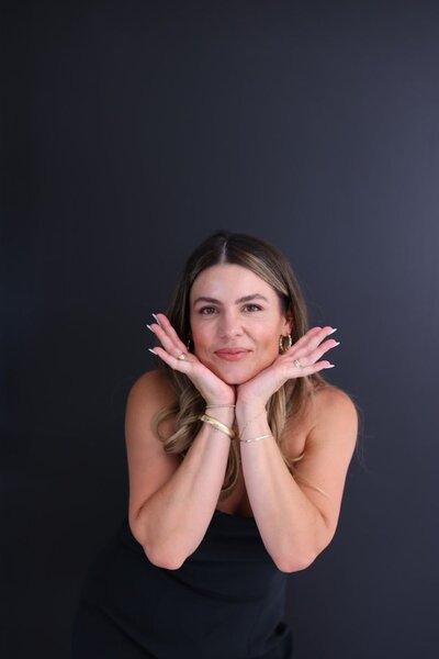 Natalie Bernacchi smiling playfully in front of a dark background, hands resting under her chin