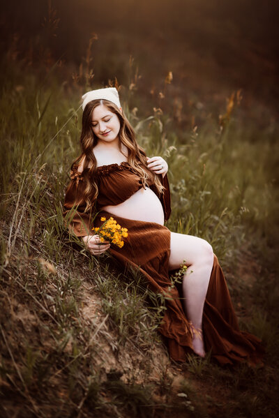 Pregnant mother holding yellow flowers sitting on grassy hill in estes park colorado