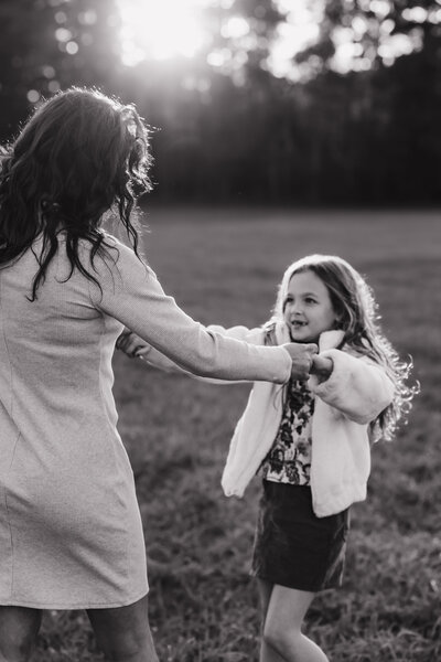 a black and white photo of a mom and daughter holding hands and spinning around