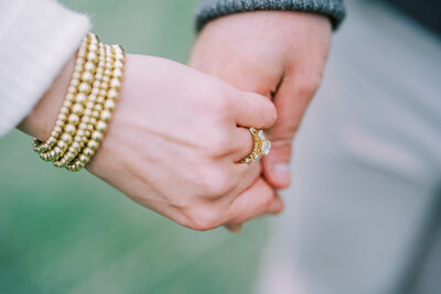 Close up image of man and woman holding hands showing off her engagement ring