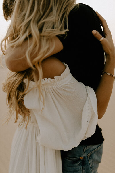 An intimate photo of a couple embracing, captured in a warm and romantic style during sunset at Silver Lake Sand Dunes.
