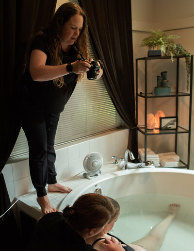 Seattle birth photographer Becky Langseth is standing over a birthing tub taking a photo of a pregnant woman about to give birth.