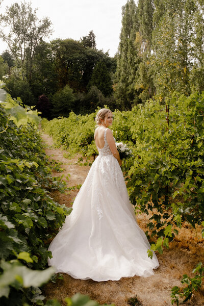 A bride standing in a field of grape vines with her bouquet