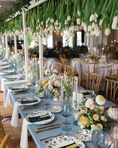 A long rectangle reception table with a blue linen and a massive tulip floral installation hanging above it draping down