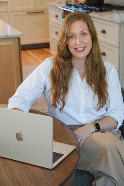 Owner and lead designer Nikki Parrish smiling at kitchen table with laptop, showcasing friendly and professional interior design service.
