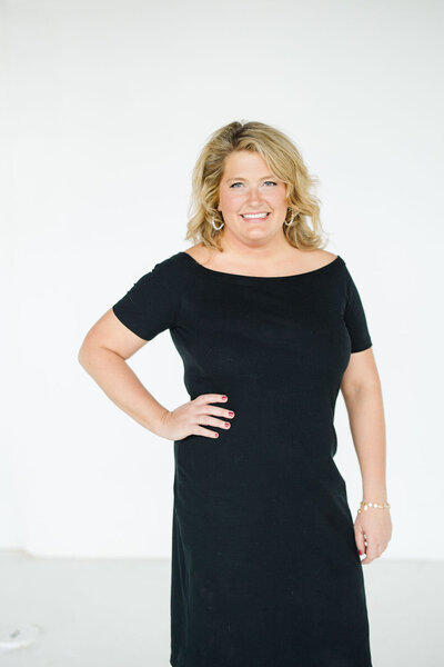 Natasha Churches, owner of Aisle & Co., poses for a headshot in all white while holding champagne.
