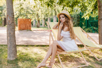 graceful-barefooted-lady-straw-hat-sitting-chaise-longue-with-pensive-face-expression-outdoor-portrait-pretty-long-haired-girl-white-dress-chilling-chair-park