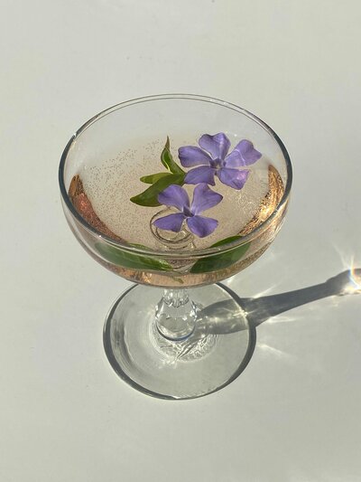 Fancy cocktail in a champagne glass and two purple flowers floating in it