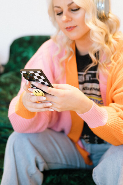 Sophie sitting on a green couch wearing headphones and looking at her phone